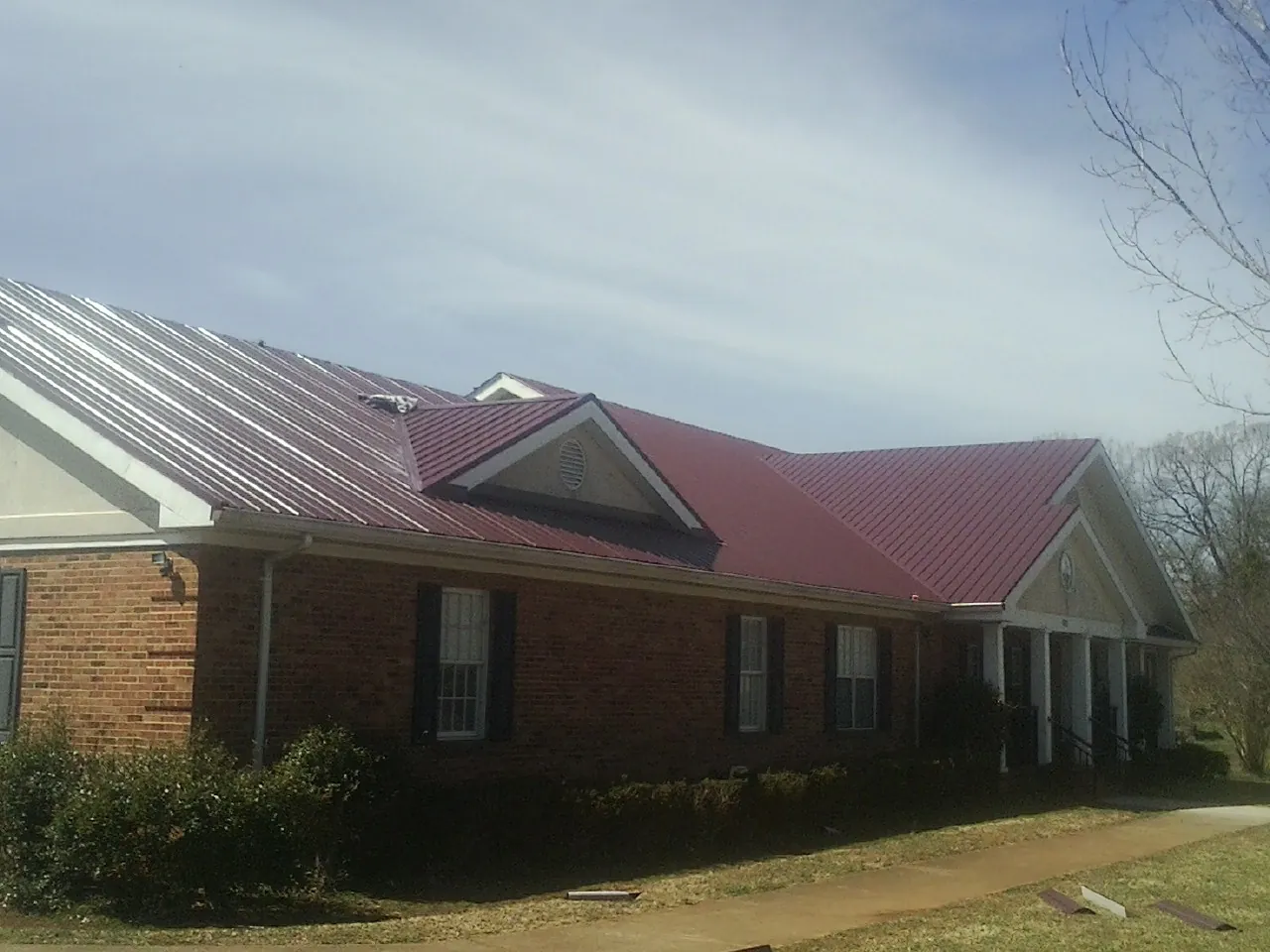 Red metal roof with gabled entries on a long brick building, from a Hail Damage Roof Repair job in Washoe Valley